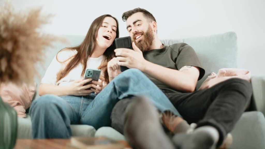 A man and woman sitting on a couch and looking at their phones.