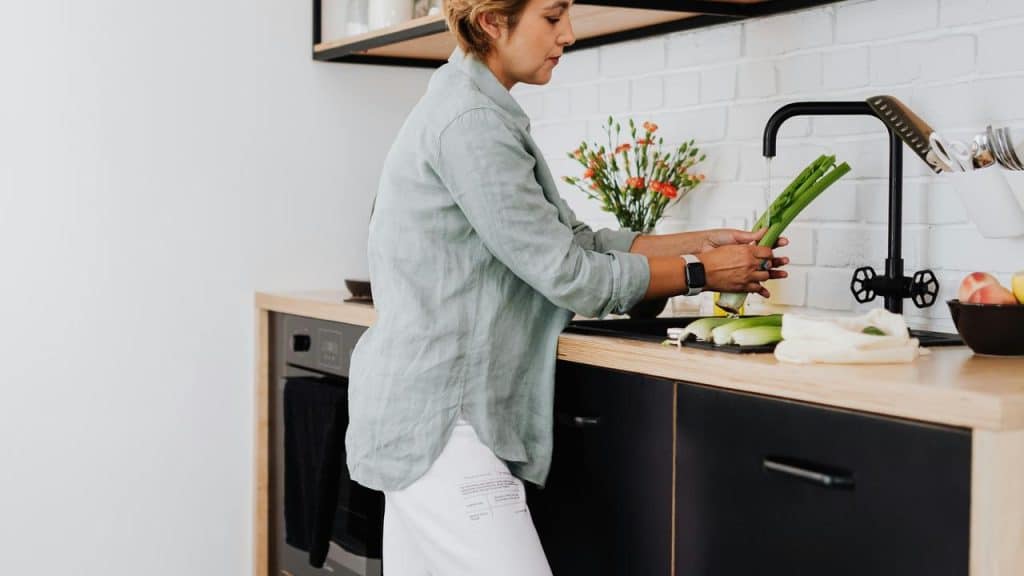 A woman washing vegetables at a kitchen sink.
