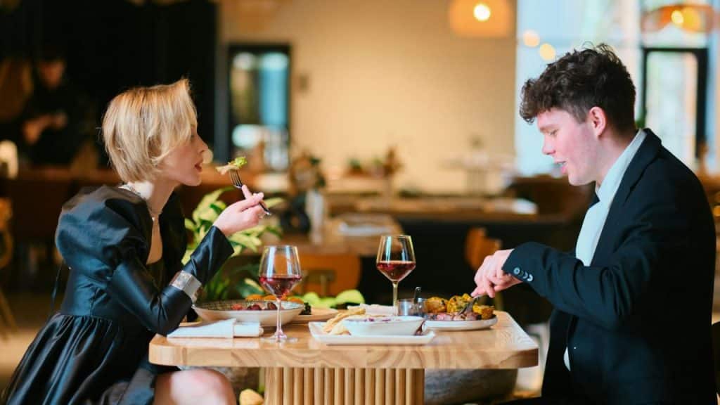 A man and woman sit at a wooden table in a restaurant eating their meal.