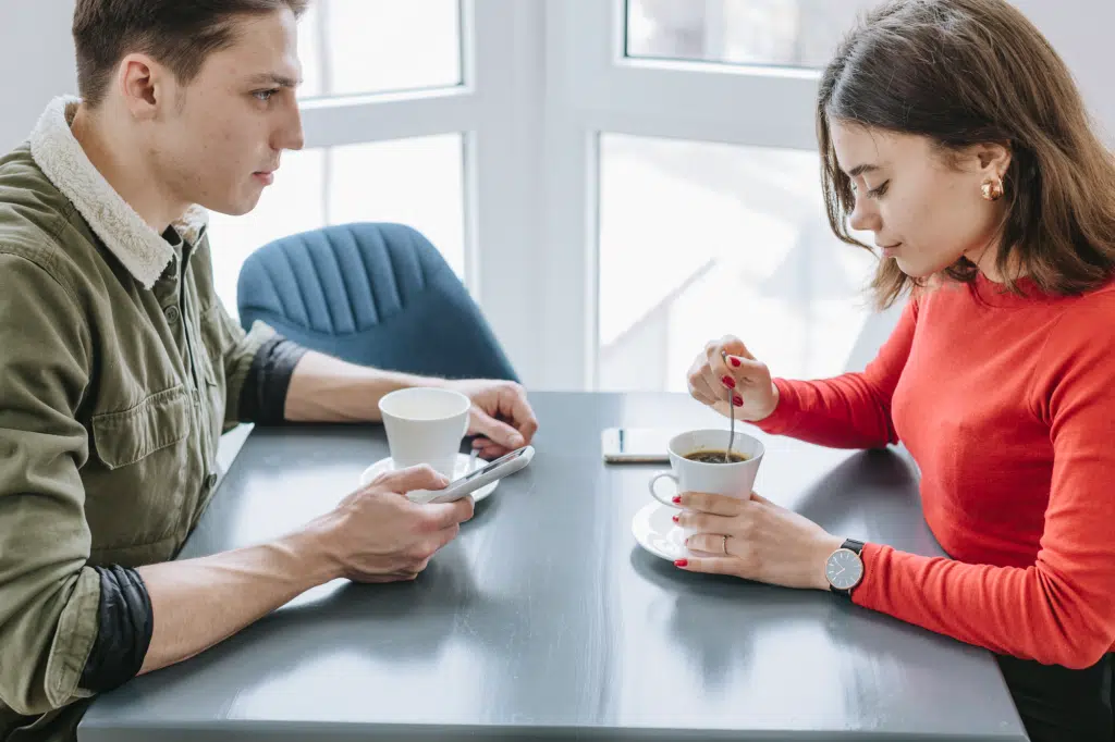 Couple having coffee in restaurant, one partner withdrawn from conversation