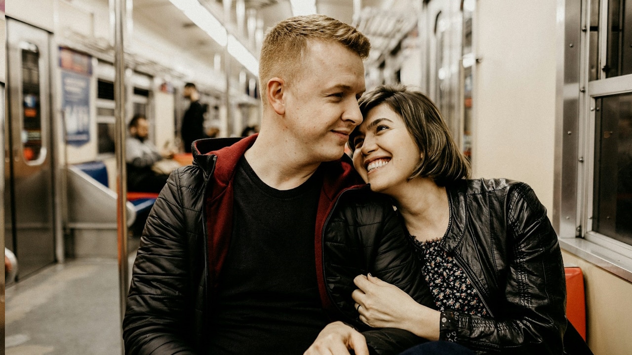 A woman holding arm of her husband while sitting in the train with him.