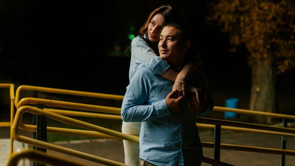 A woman hugging a man from behind as they stand outdoors at night.