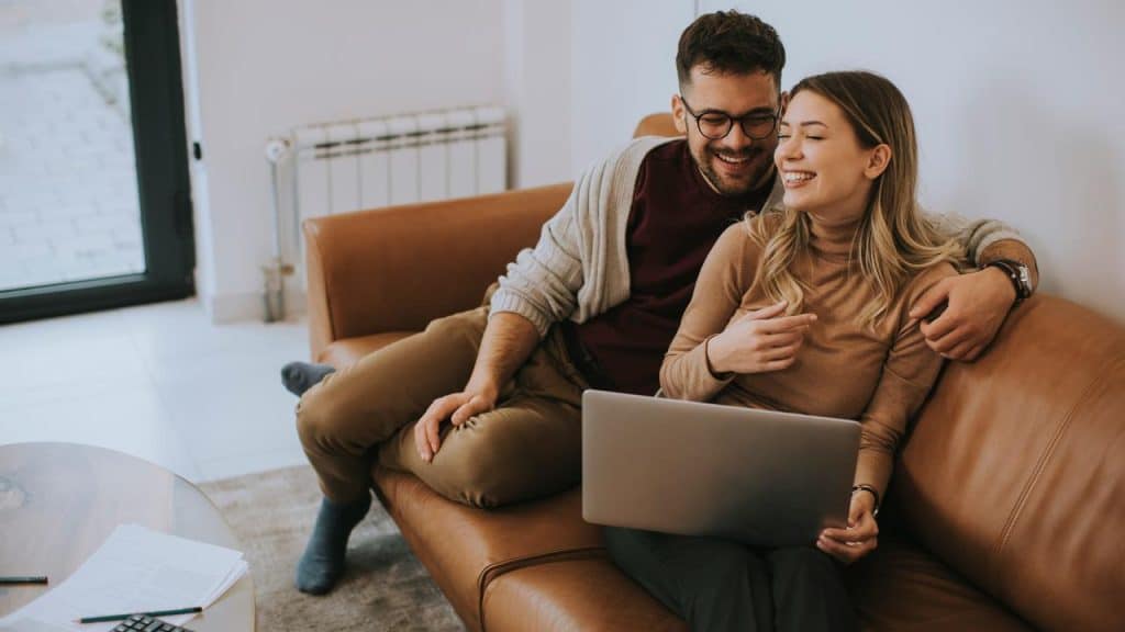 A couple on a couch looking at a laptop and laughing.