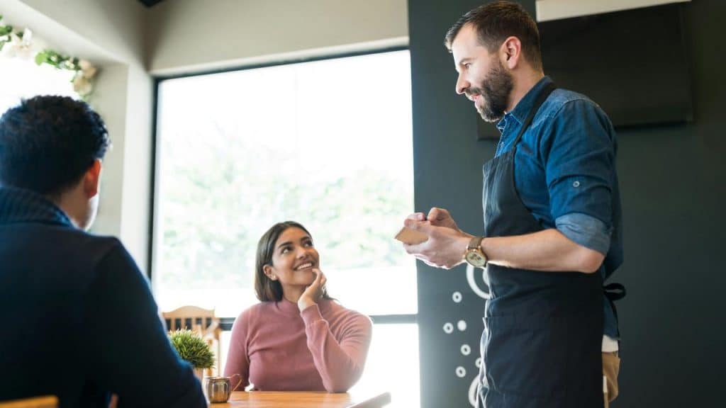 A smiling waitress taking an order from a couple at a restaurant.
