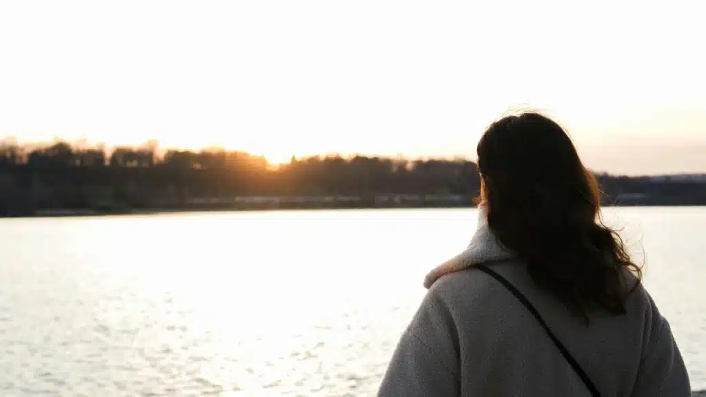 A person standing by a lake at sunset, looking across the water.