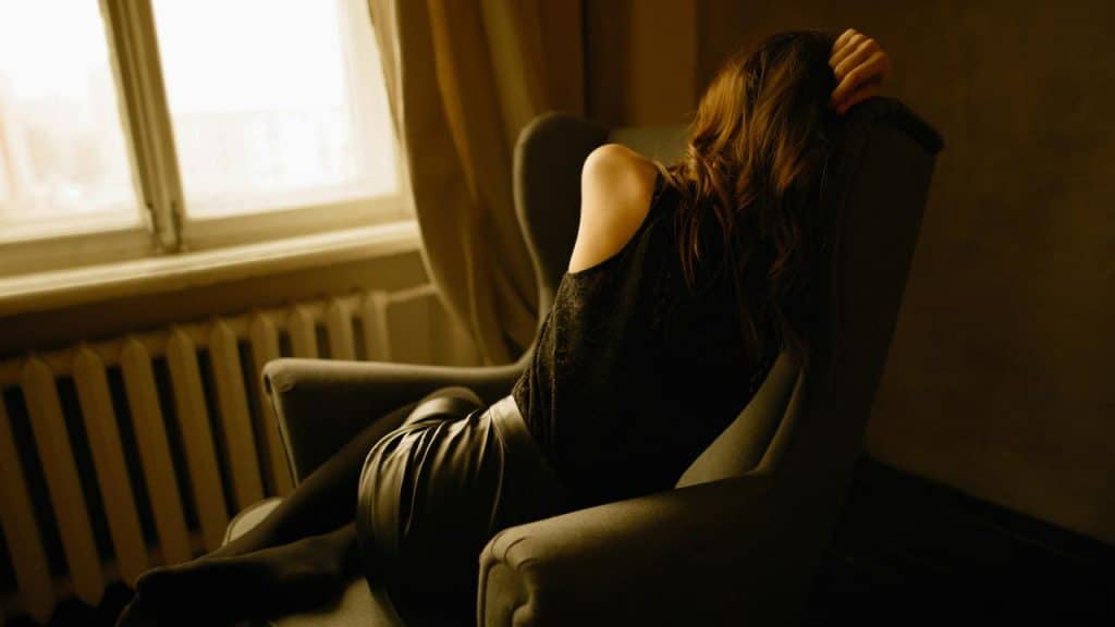 A person reclining in an armchair near a window with their head resting on their hand.