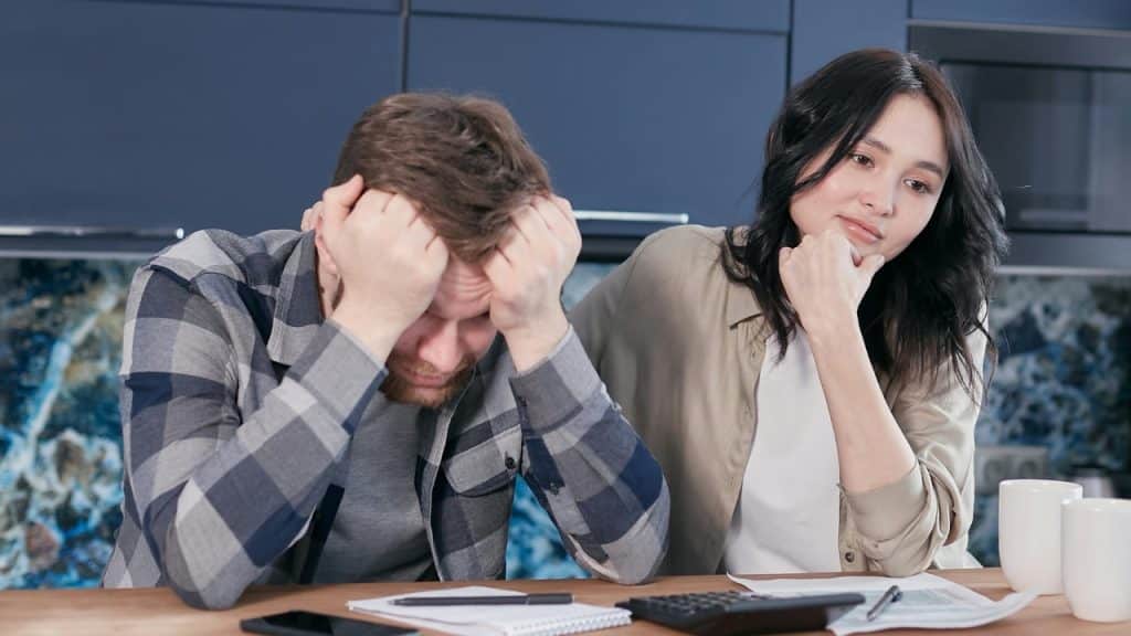 A man rests his head in his hands while a woman sits nearby watching him.
