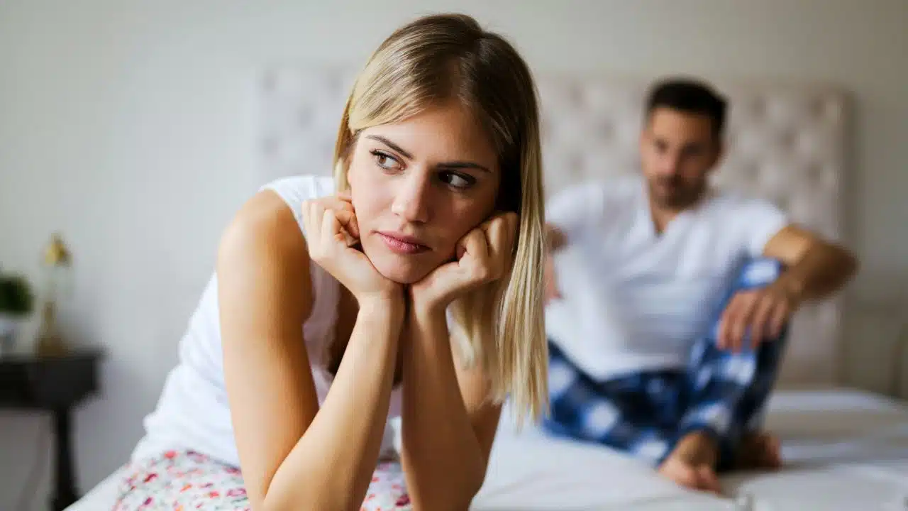 A woman rests her chin on her hands with a worried expression while a man sits behind.
