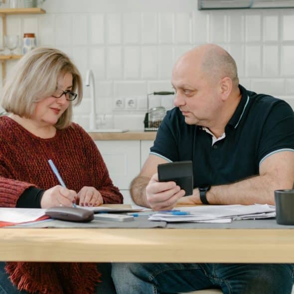 A man and woman sit at a kitchen table reviewing several papers and a calculator.