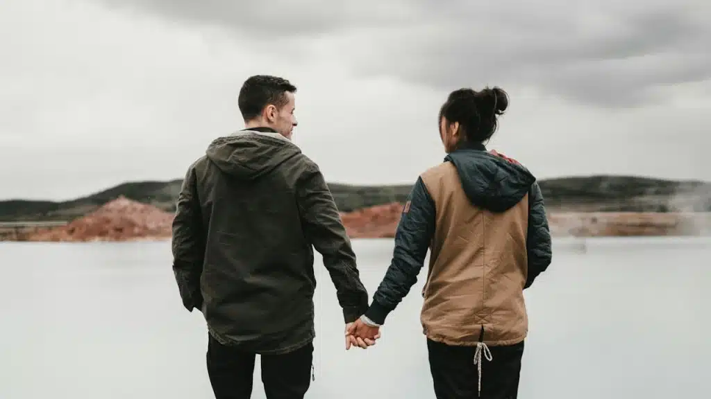 A couple holding hands in front of a lake.