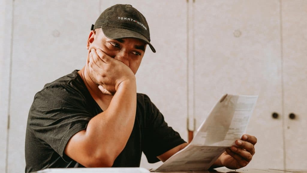 A man wearing a black baseball cap rests his hand on his face while reading a paper.