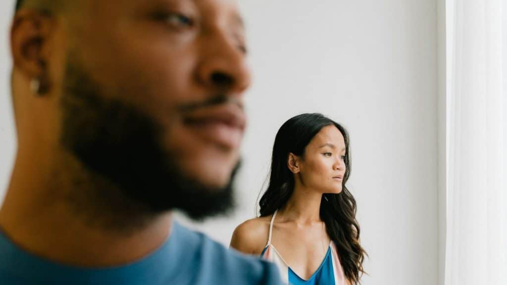 A blurred man's face is in the foreground, with a woman in a colorful top looking away in the background.