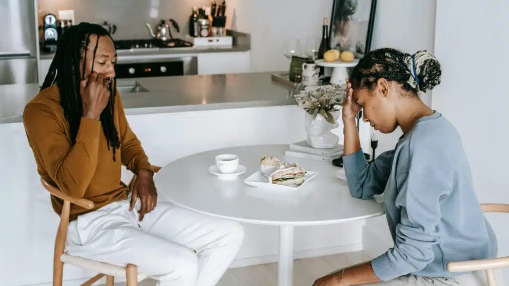 A man and a woman sit at a round table with food and drinks.