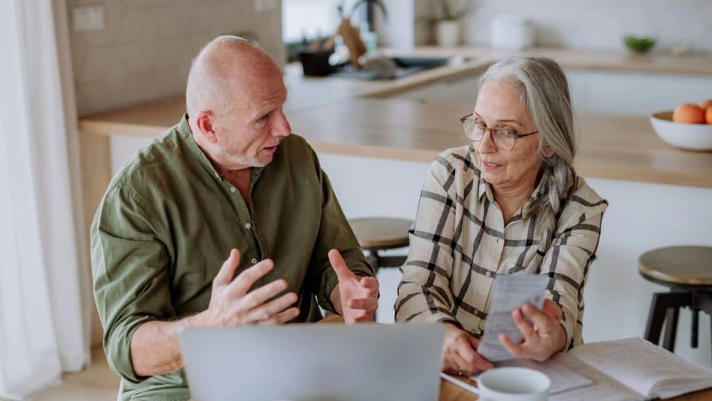 An older man and woman sit at a table looking at a paper together.