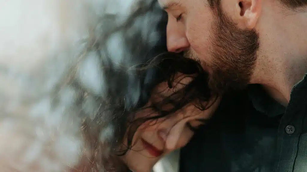 A man gently kissing a woman’s head as they embrace.