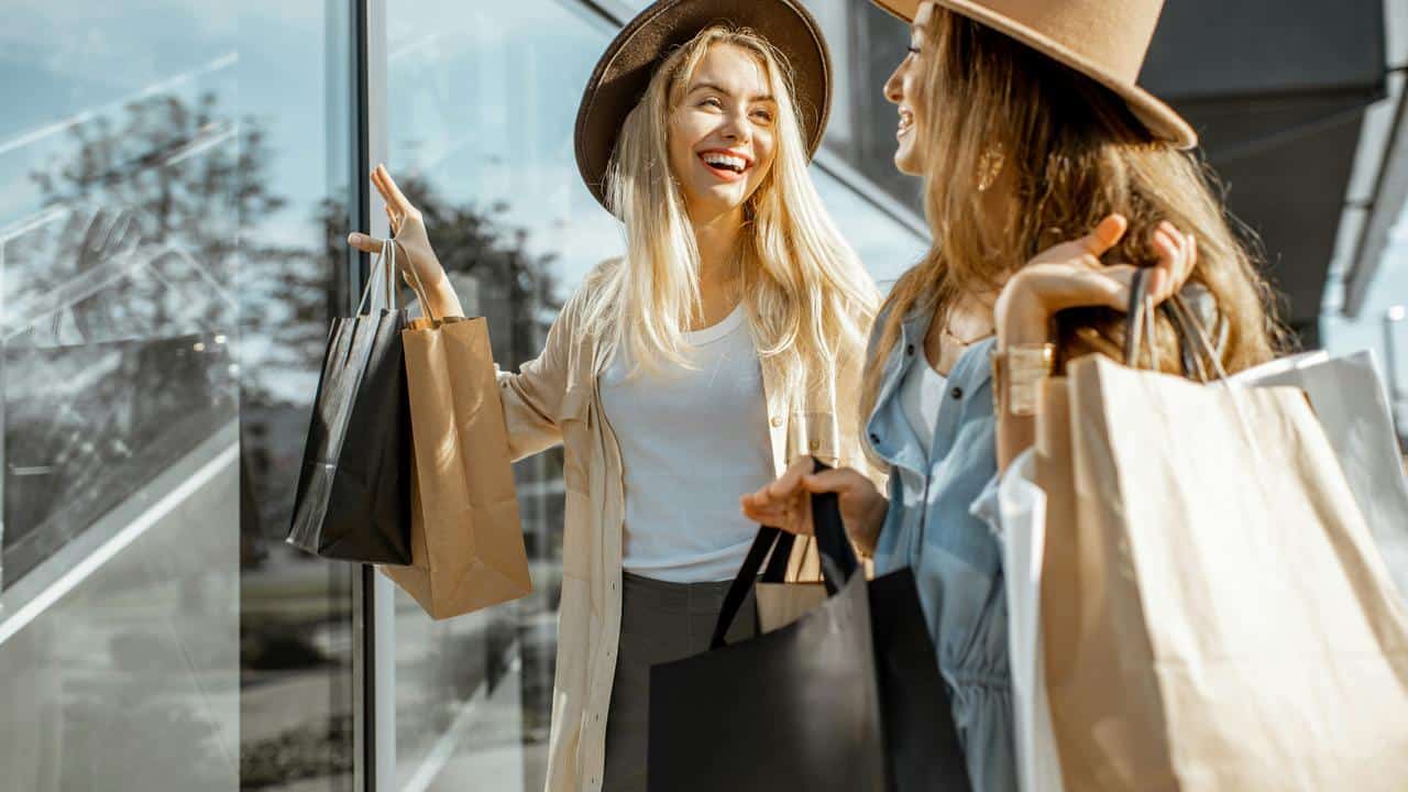A pair of women laughing and holding shopping bags outside a store.