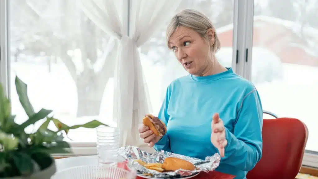 A woman gestures while holding a sandwich at a table