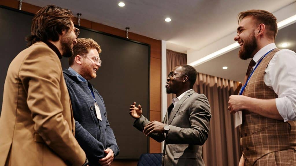 Four men in professional attire stand in a circle talking and smiling indoors.