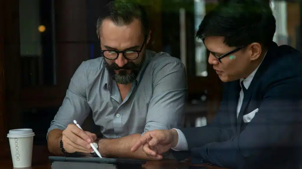 A man with a beard and a man in a suit use a tablet together.