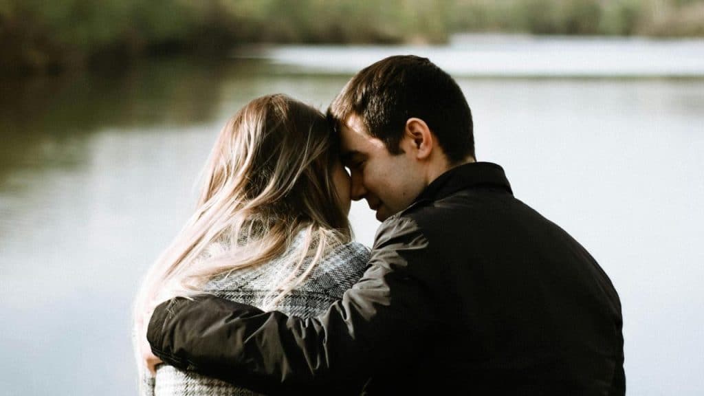 A couple embracing beside a calm lake.