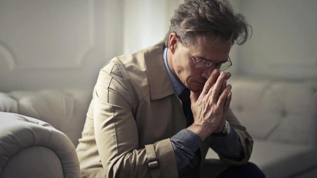 A man sitting with hands clasped, looking stressed.