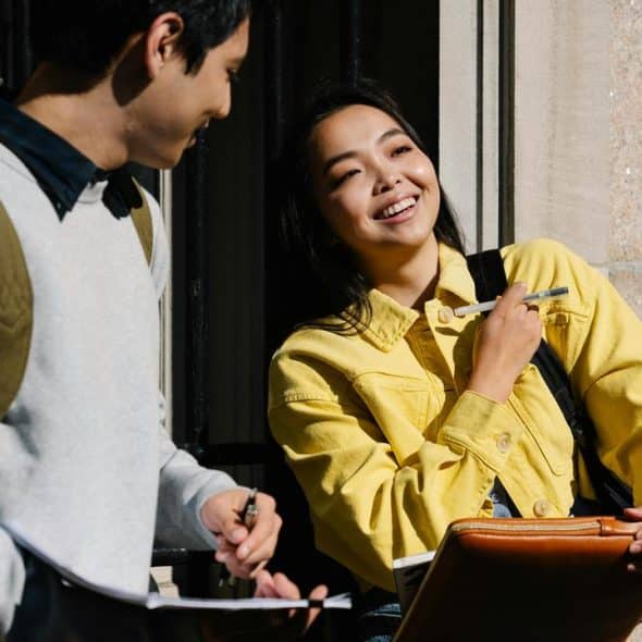 A smiling woman in a yellow jacket chatting with a guy outside.