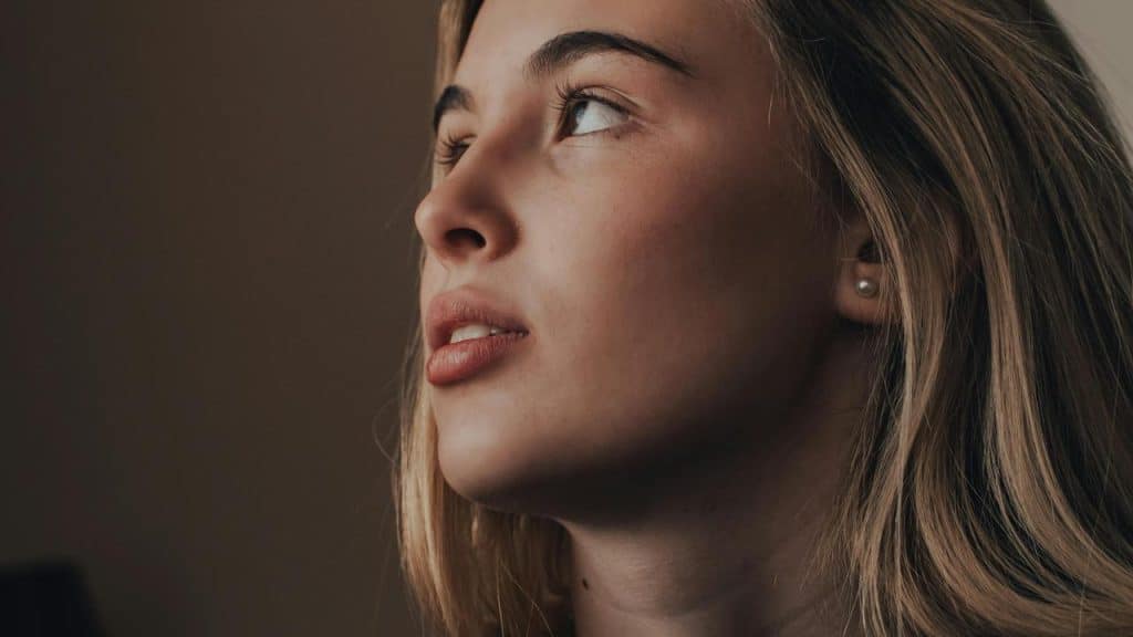 A close-up of a woman looking upward with a thoughtful expression.