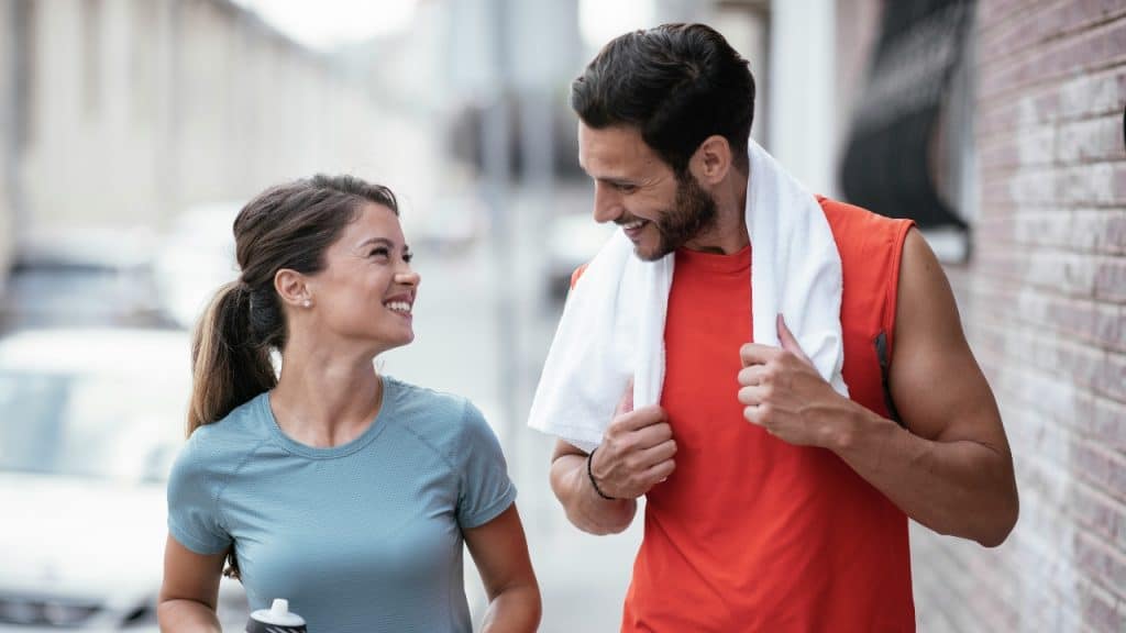 A man with a towel around his neck smiles at a woman in athletic wear.