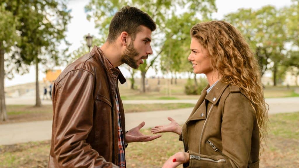 A man and a woman in a park gesture with their hands while talking to each other.