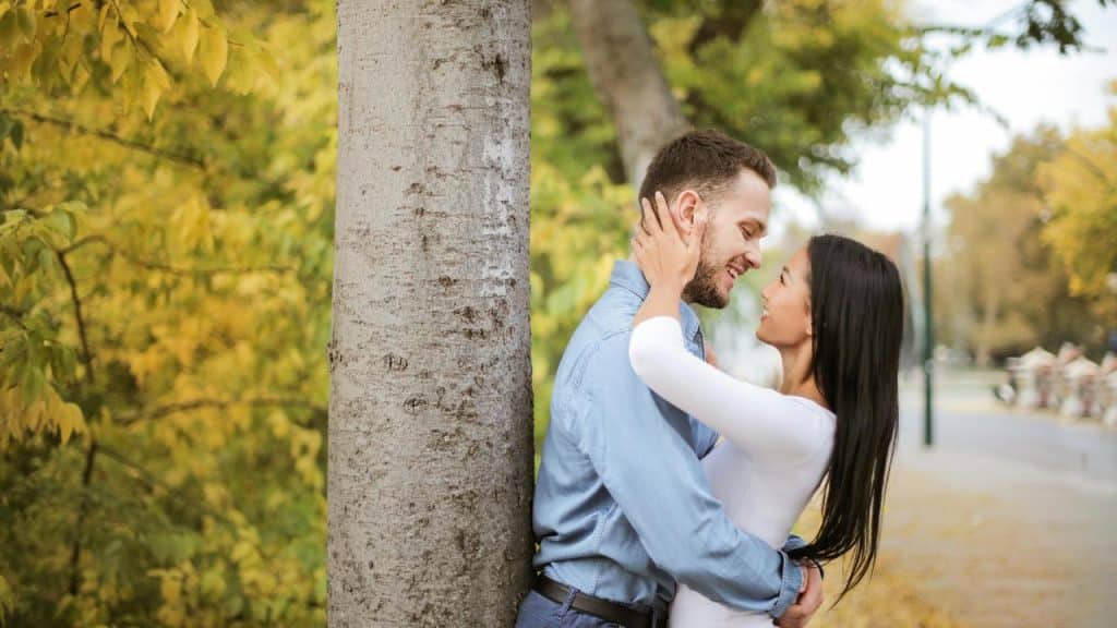 A couple embracing beside a tree in a park.