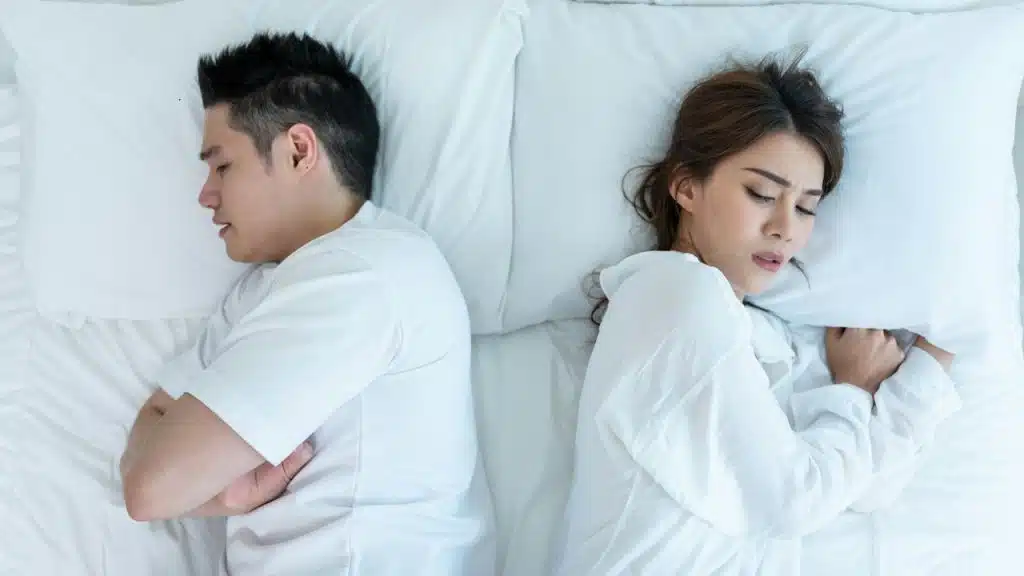 A man and woman turned their faces after a quarrel while lying on a bed together.