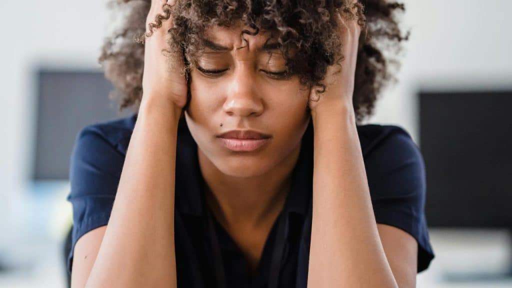 A woman holding her head with eyes closed, looking stressed or overwhelmed.
