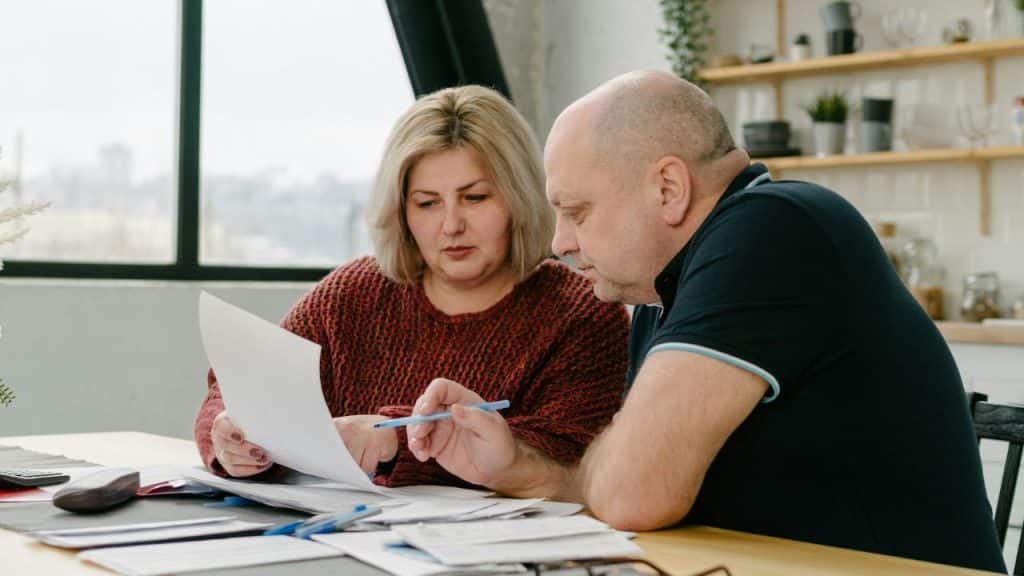 A woman and man sit at a table reviewing paperwork together with pens.
