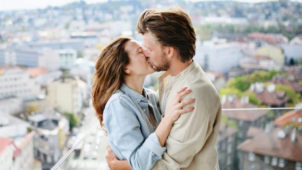 A man and woman sharing a kiss while standing on a high balcony.