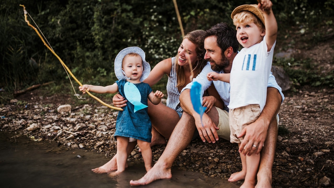 A couple playing with their kids and sitting with their feet soaking in a pond.