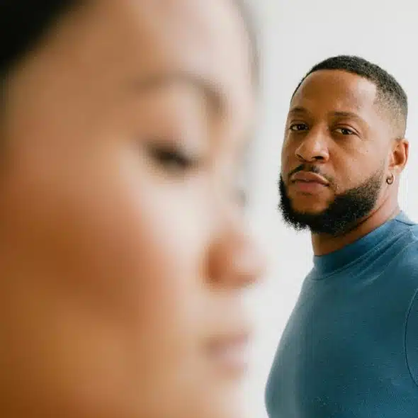 A bearded man in a blue shirt looks forward while a woman is blurred in foreground.