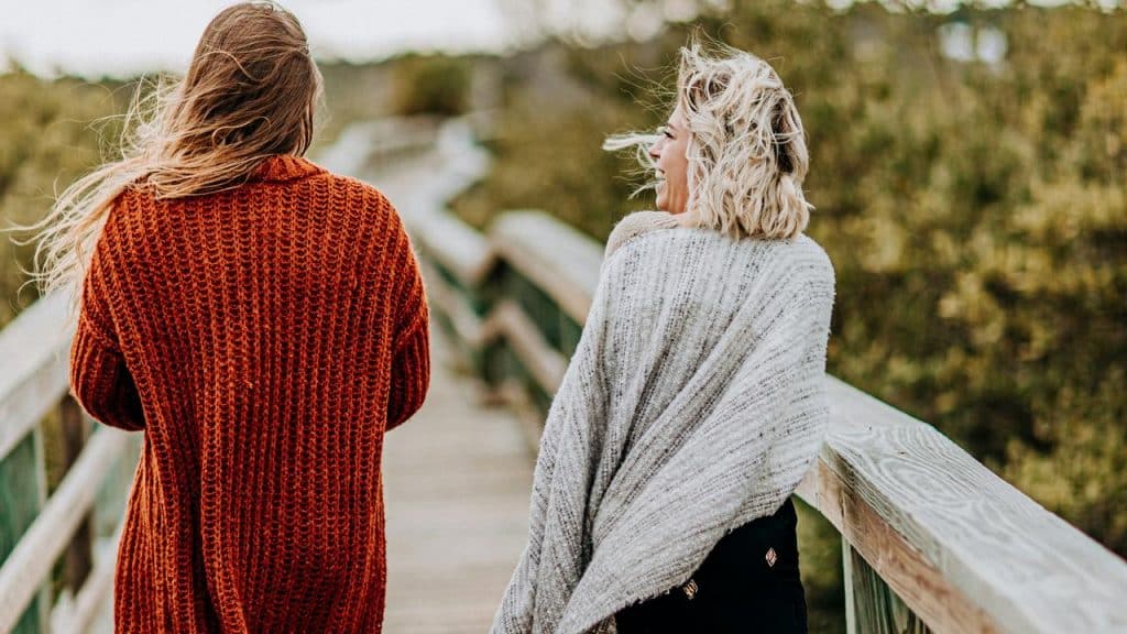 A pair of women walking together on a wooden boardwalk outdoors.