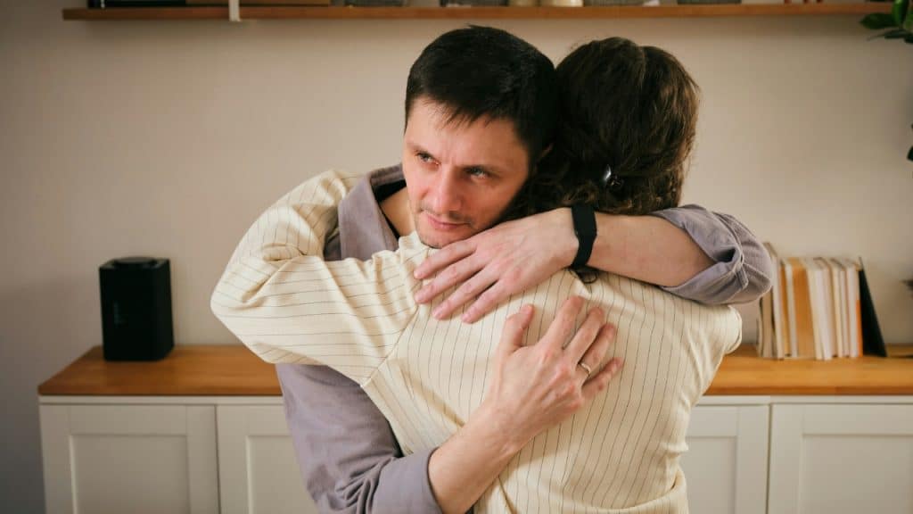 A man with a somber expression hugs a woman whose back is to the camera.
