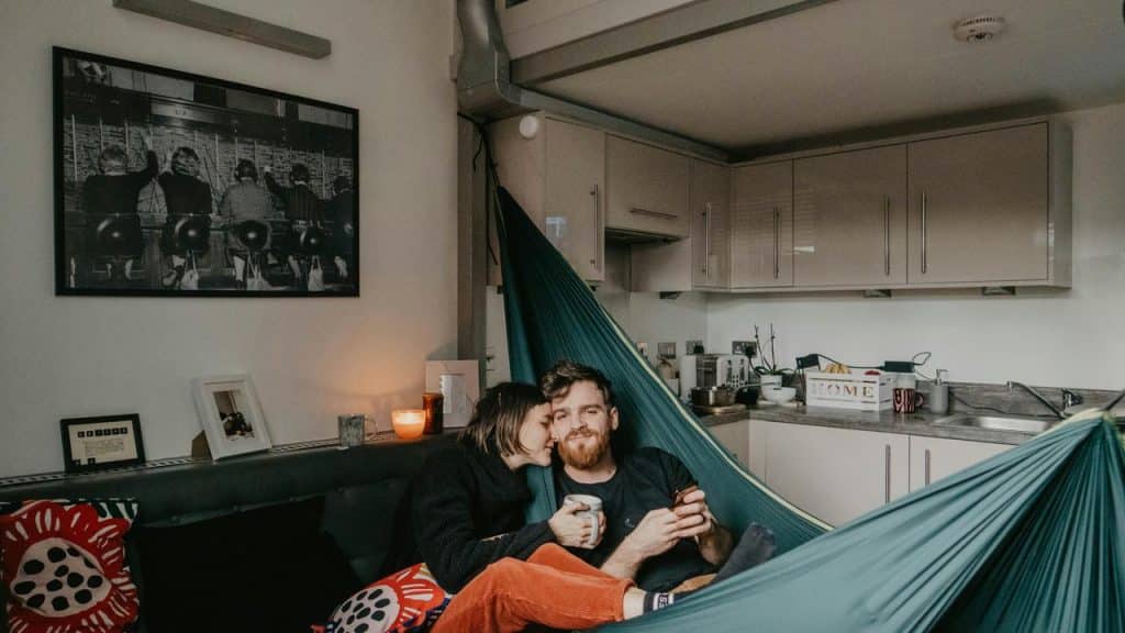 A couple cuddling in a hammock inside a cozy apartment kitchen.