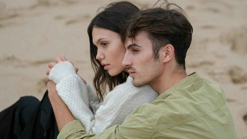 A couple sitting on a beach close to each other.