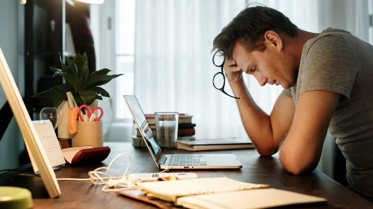 A man holds his glasses and leans his head on his hand at a desk.