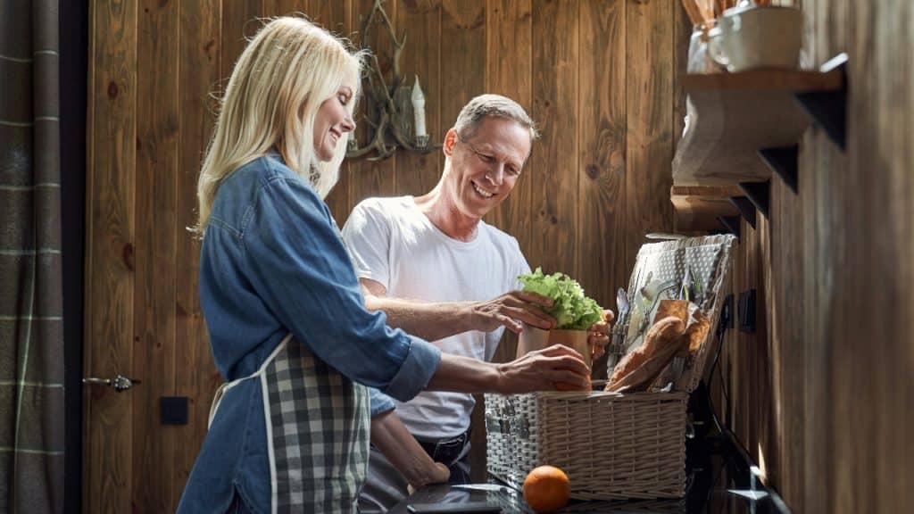 A man and woman smile while standing in a kitchen with a wicker picnic basket.