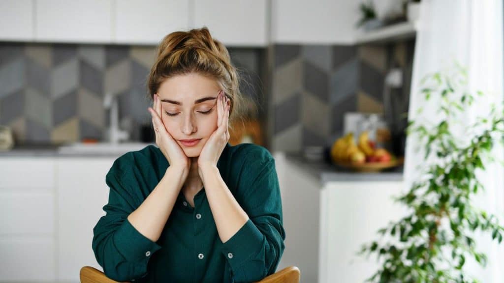 A woman sitting at a table with her head resting in her hands, looking tired or stressed.