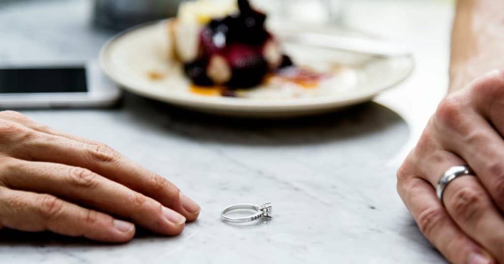 A ring resting on a table between two people’s hands.