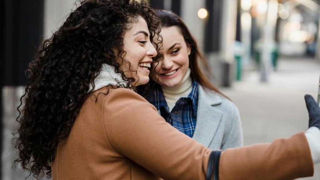 A pair of women smiling and taking a selfie together on a city street.