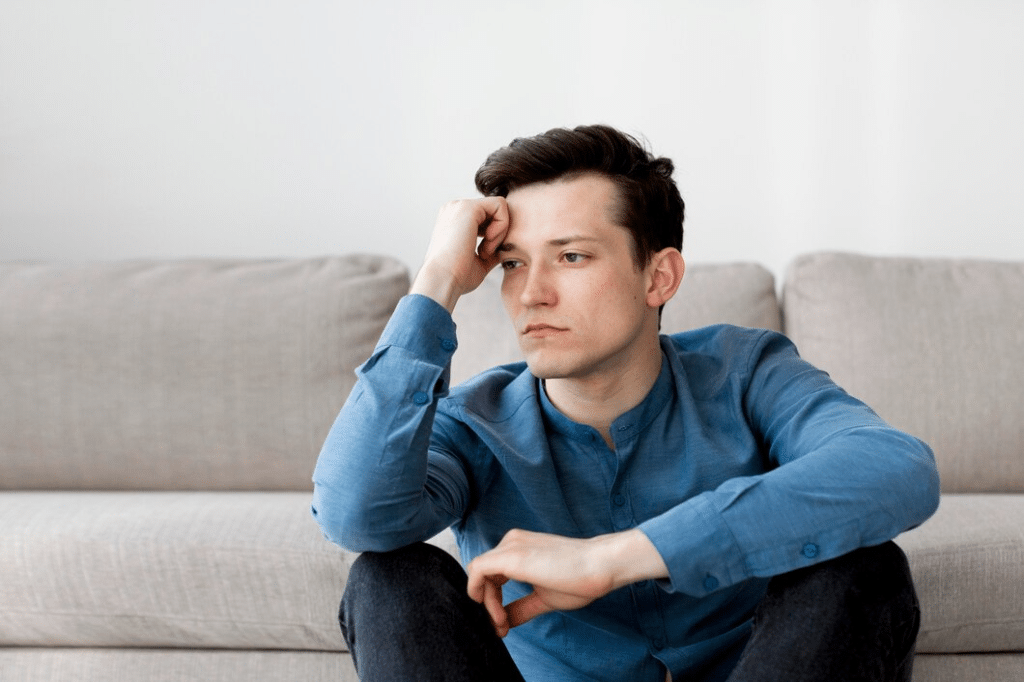 Man upset sitting down in front of sofa