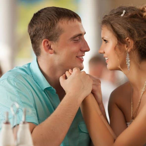 A man and woman in a restaurant hold hands and smile at each other.