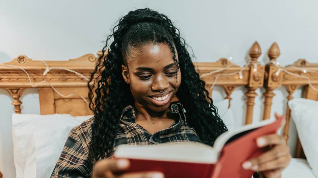 A woman sitting on a bed reading a book.