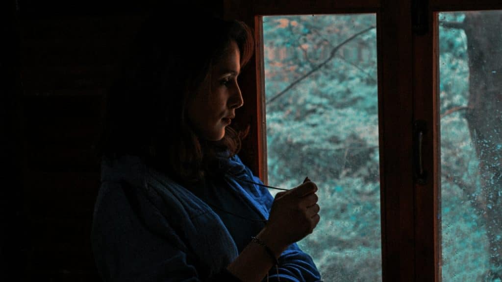 A woman sits in shadow near a window, holding a thin cord in her hands.