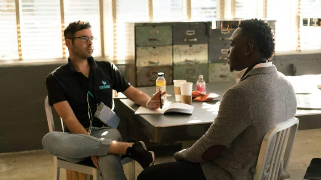Two men sit across from each other at a table with coffee and notebooks.
